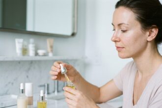 Femme appliquant un sérum visage devant son miroir de salle de bain, choisissant parmi plusieurs flacons de sérums skincare