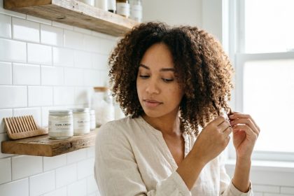 Jeune femme aux cheveux bouclés naturels appliquant de la crème coiffante dans une salle de bain moderne, routine d'entretien des boucles