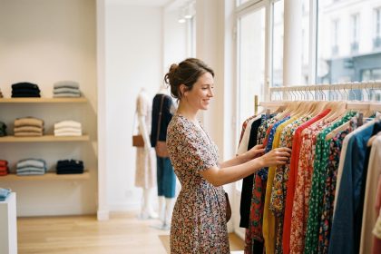 Femme souriante feuilletant des robes dans une boutique parisienne lumineuse, illustrant la tendance des robes dans la mode féminine